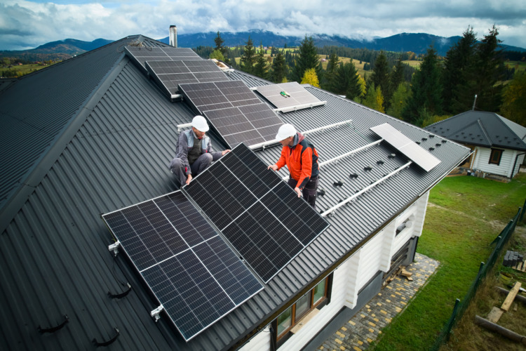 Engineers building photovoltaic solar module station on roof of house. Men electricians in helmets installing solar panel system outdoors. Concept of alternative and renewable energy.